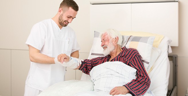 Pfleger am Bett eines Patienten (wird nicht ausgespielt, wichtig für blinde Menschen)