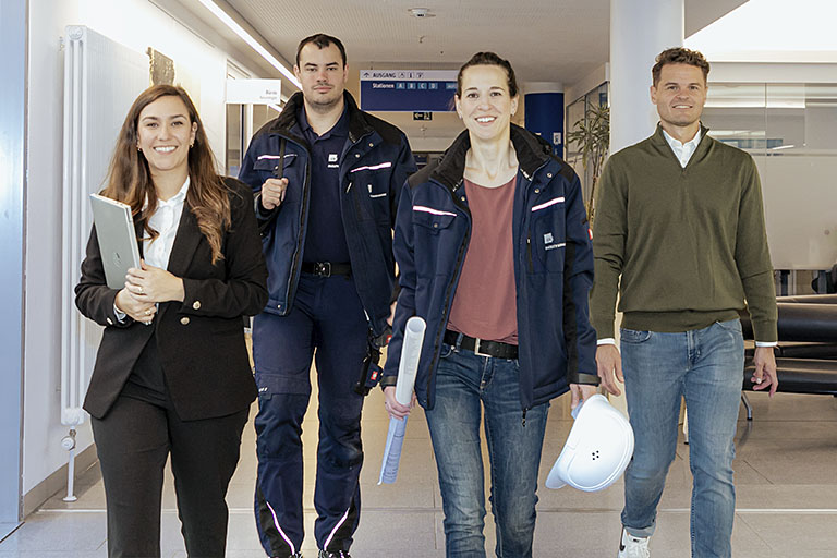 Arbeiten bei der KFE - Mitarbeitende der KFE laufen auf dem Gang auf den Fotografen zu